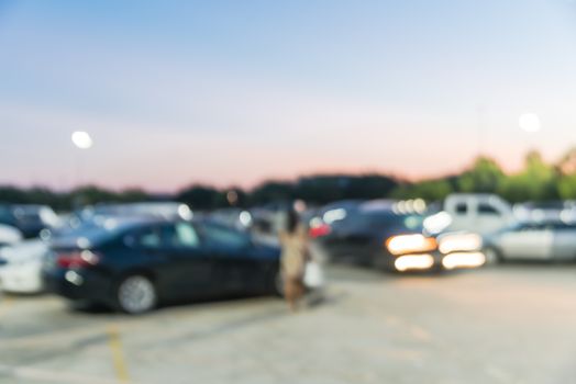 Motion blurred customer out shopping in holidays season at modern shopping center in Humble, Texas, US. Busy outdoor parking lots at sunset, mall complex uncovered parking with light lampposts