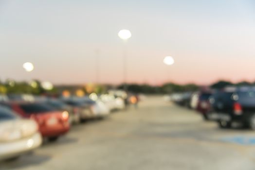 Abstract blurred parking lot of modern shopping center in Houston, Texas, USA. Exterior view mall complex with row of cars in outdoor uncovered parking, bokeh light poles in background