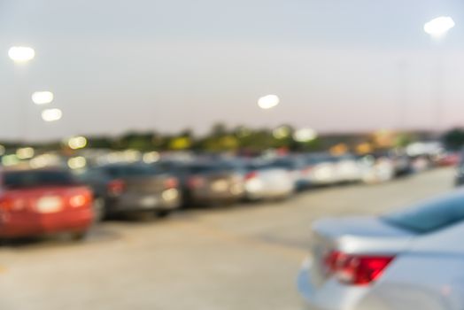 Abstract blurred parking lot of modern shopping center in Houston, Texas, USA. Exterior view mall complex with row of cars in outdoor uncovered parking, bokeh light poles in background