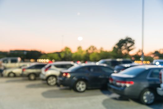 Abstract blurred parking lot of modern shopping center in Houston, Texas, USA. Exterior view mall complex with row of cars in outdoor uncovered parking, bokeh light poles in background