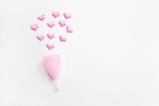 Pink menstrual cup on white background with small hearts. Concept zero waste, savings, environmental conservation, sustainable lifestyle. Feminine hygiene product, flatlay, copy space. Horizontal.