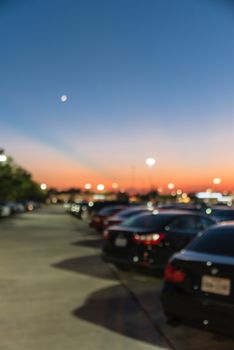 Abstract blurred parking lot of modern shopping center in Houston, Texas, USA. Exterior view mall complex with row of cars in outdoor uncovered parking, bokeh light poles in background