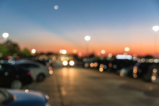 Abstract blurred parking lot of modern shopping center in Houston, Texas, USA. Exterior view mall complex with row of cars in outdoor uncovered parking, bokeh light poles in background