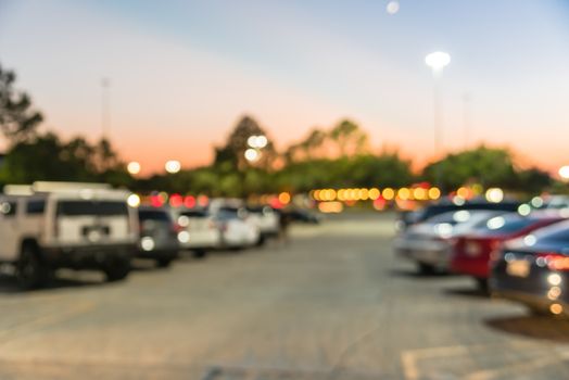 Abstract blurred parking lot of modern shopping center in Houston, Texas, USA. Exterior view mall complex with row of cars in outdoor uncovered parking, bokeh light poles in background