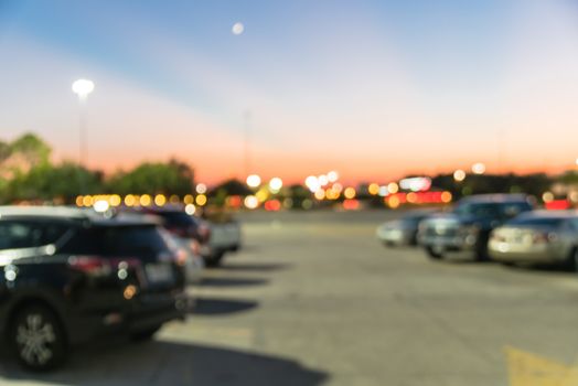 Blurred abstract retail store facade of modern shopping center in Humble, Texas, US at sunset. Mall complex with row of cars in outdoor uncovered parking lots with light poles in background