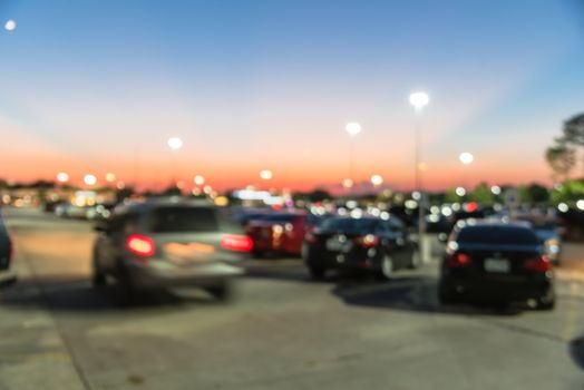 Abstract blurred parking lot of modern shopping center in Houston, Texas, USA. Exterior view mall complex with row of cars in outdoor uncovered parking, bokeh light poles in background