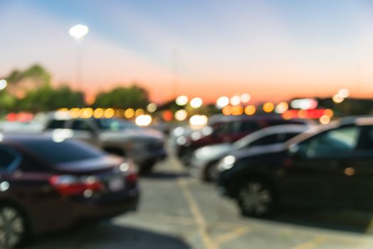 Abstract blurred parking lot of modern shopping center in Houston, Texas, USA. Exterior view mall complex with row of cars in outdoor uncovered parking, bokeh light poles in background