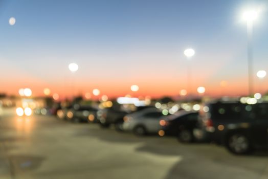 Blurred abstract retail store facade of modern shopping center in Humble, Texas, US at sunset. Mall complex with row of cars in outdoor uncovered parking lots with light poles in background