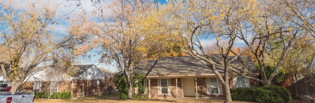 Panorama view typical bungalow style house in Dallas, Texas suburbs during fall season with colorful autumn leaves. Middle class neighborhood single story residential home with mature tree