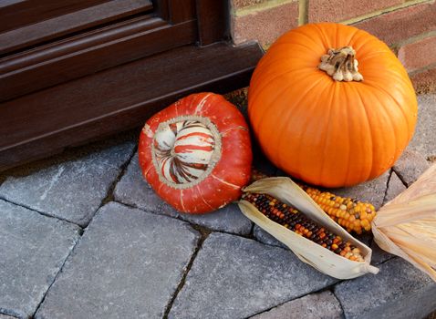 Turks Turban gourd with colourful ornamental corn and large orange pumpkin as Thanksgiving decorations on a stone doorstep with copy space