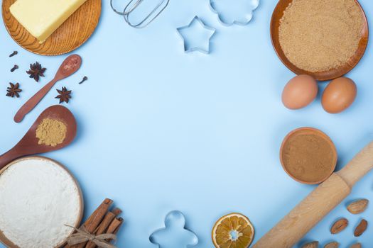 Christmas gingerbread cookies cooking background flat lay top view template with copy space for text. Baking utensils, spices and food ingredients on blue background