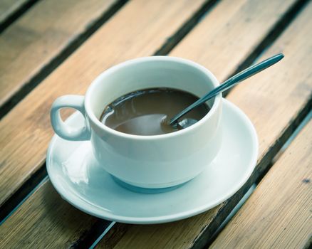 Toned photo of Popular Vietnamese milk coffee in ceramic cup and saucer with stainless spoon on outdoor wooden table. Top view a morning Vietnamese gourmet drink. Food concept.