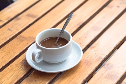 Popular Vietnamese milk coffee in ceramic cup and saucer with stainless spoon on outdoor wooden table. Top view a morning Vietnamese gourmet drink. Food concept.