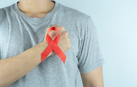 Aids awareness, male hands holding red AIDS awareness ribbon. World Aids Day, Healthcare and medical concept.