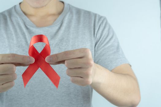 Aids awareness, male hands holding red AIDS awareness ribbon. World Aids Day, Healthcare and medical concept.