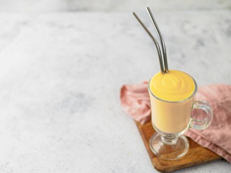 Yellow mango yogurt or smoothie on gray cement background with copy space left. Turmeric Lassie or lassi in glass with metal straws
