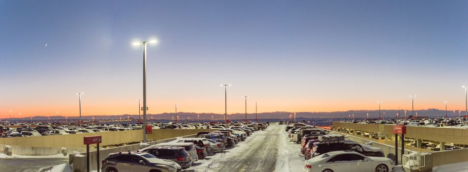 Panorama view full terminal parking at Denver International Airport (DIA) in frosty cold autumn sunset. Row of cars at busy lot with snowdrifts during severe weather condition in Colorado, USA