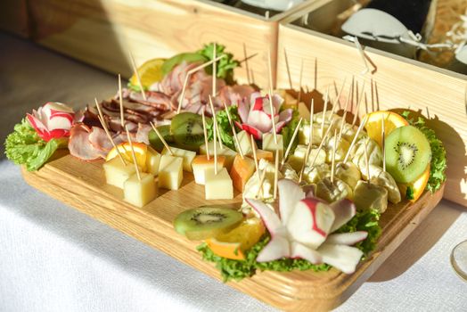 A widely varied food with coctail sticks on wooden plate, harsh sun light.