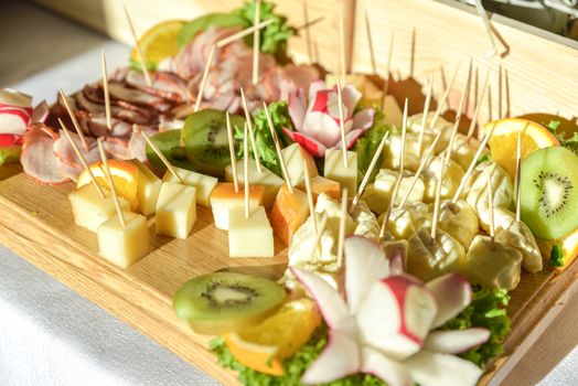 A widely varied food with coctail sticks on wooden plate, harsh sun light.