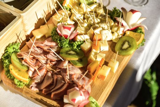 A widely varied food with coctail sticks on wooden plate, harsh sun light.