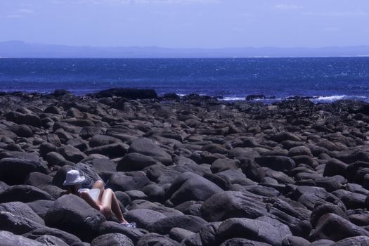 Relaxed girl reading a book on the seashore rocks by the ocean, St. Francis Bay, South Africa