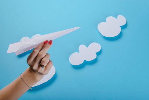 Paper plane in female hand on a blue background with clouds