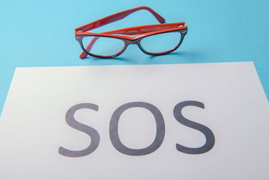 Word SOS written on white paper. Blue background