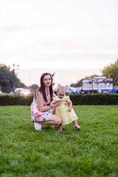 Happy mother and daughter in the park. Beauty nature scene with family outdoor lifestyle. Happy family resting together on the green grass, having fun outdoor. Happiness and harmony in family life.