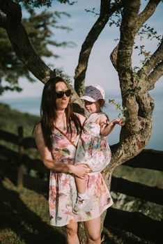 Happy mother and daughter in the park. Beauty nature scene with family outdoor lifestyle. Happy family resting together on the green grass, having fun outdoor. Happiness and harmony in family life.