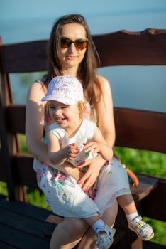 Happy mother and daughter in the park. Beauty nature scene with family outdoor lifestyle. Happy family resting together on the green grass, having fun outdoor. Happiness and harmony in family life.