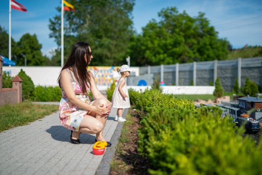 Happy mother and daughter in the park. Beauty nature scene with family outdoor lifestyle. Happy family resting together on the green grass, having fun outdoor. Happiness and harmony in family life.