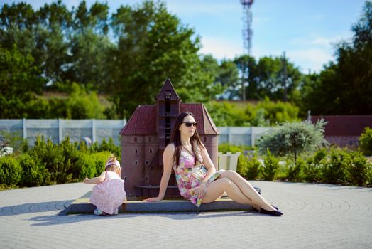Happy mother and daughter in the park. Beauty nature scene with family outdoor lifestyle. Happy family resting together on the green grass, having fun outdoor. Happiness and harmony in family life.
