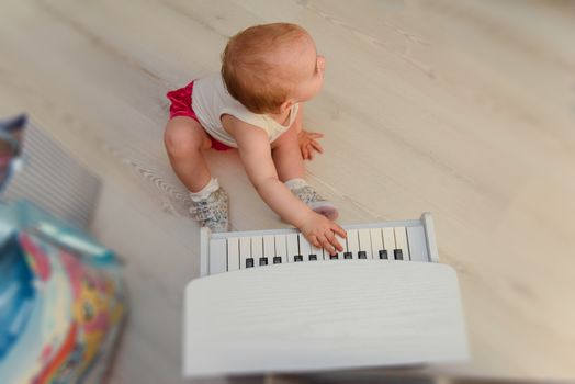 beautiful baby girl playing toy piano in light room. Authentic image.
