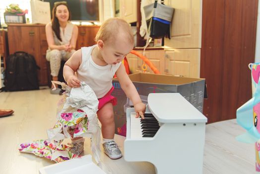 beautiful baby girl playing toy piano in light room. Authentic image.