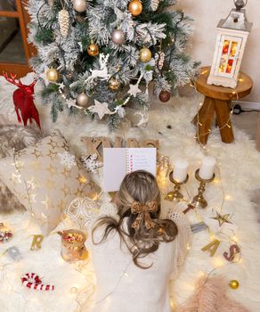 Woman makes her Christmas shopping list while lying in front of the Christmas tree with Chiristmas decorations all around her