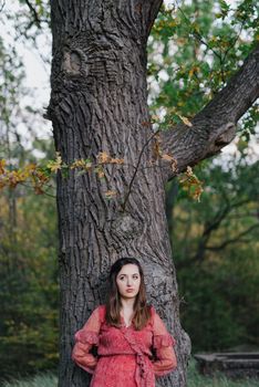 Woman standing next to a tree in park in golden autumn.
