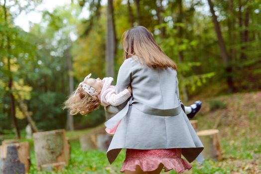 Mother holds daughter in her arms in the park on a sunny day. Autumn day