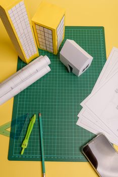White family paper house over block of flats on yellow background paper. Minimalistic and simple concept, style. Copy space. Vertical orientation.