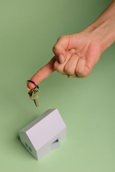 White family paper house. House keys in hand on mint background paper. Minimalistic and simple concept, style. Copy space. Vertical orientation. Family moving or removal concept.