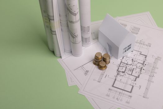 White family paper house , stack of money coins, house projects plan and blueprints on mint background paper. Minimalistic and simple concept, style. Vertical orientation