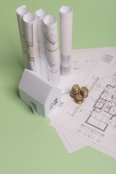 White family paper house , stack of money coins, house projects plan and blueprints on mint background paper. Minimalistic and simple concept, style. Vertical orientation