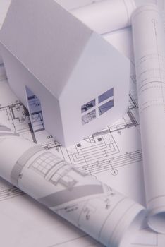 White family paper house, house projects plan and blueprints in the background. Minimalistic and simple concept, style. Horizontal orientation. View from above.