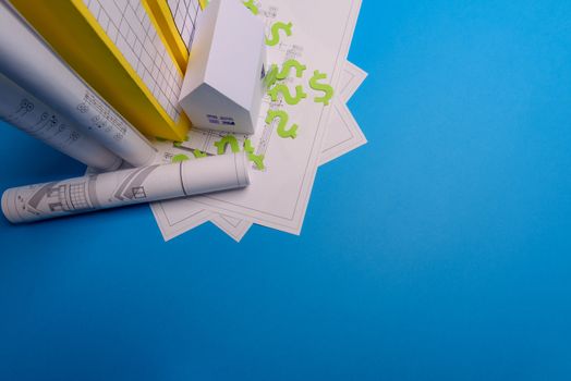 Paper skyscrapers , us dollar money, house projects plan and blueprints on blue background paper. Minimalistic and simple concept, style. Horizontal orientation. View from above. Copy space.