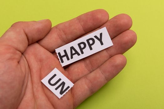 man hand holding card with text unhappy, cutting word 'un' so it written 'happy'. Copy space. Lime background. Studio shoot.