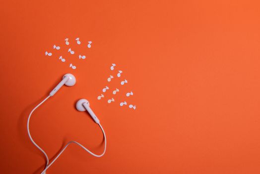 white earphones and white paper notes on orange background. view from above