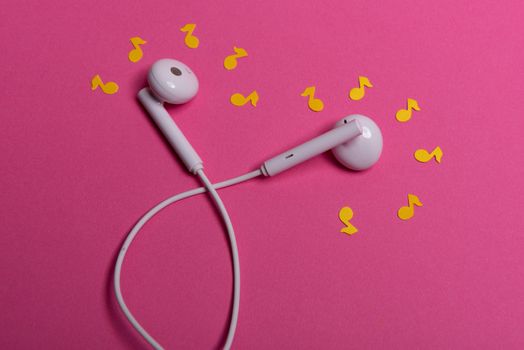 white earphones and yellow paper notes on pink background. view from above