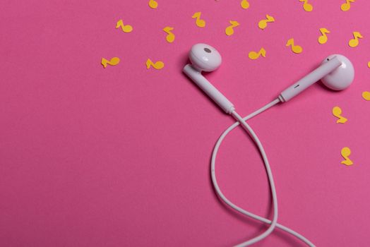 white earphones and yellow paper notes on pink background. view from above