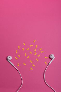 white earphones and yellow paper notes on pink background. view from above