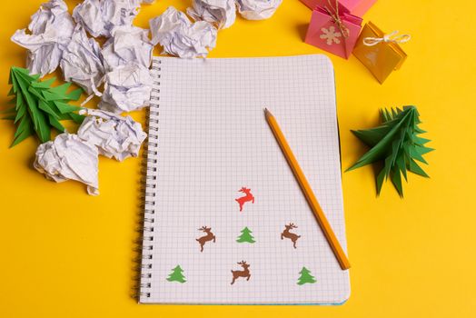 gift box and green paper origami trees with notepad on yellow desk, table. Christmas to do list text.