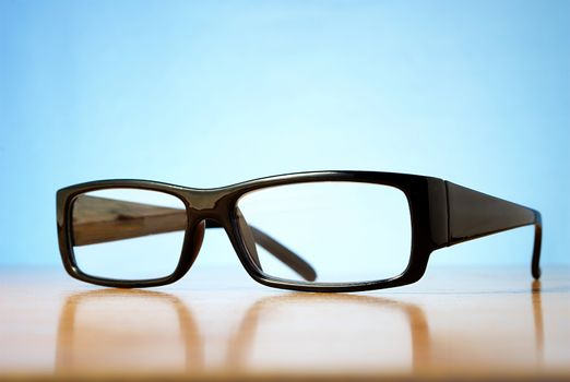 black-rimmed glasses on a table and a blue background